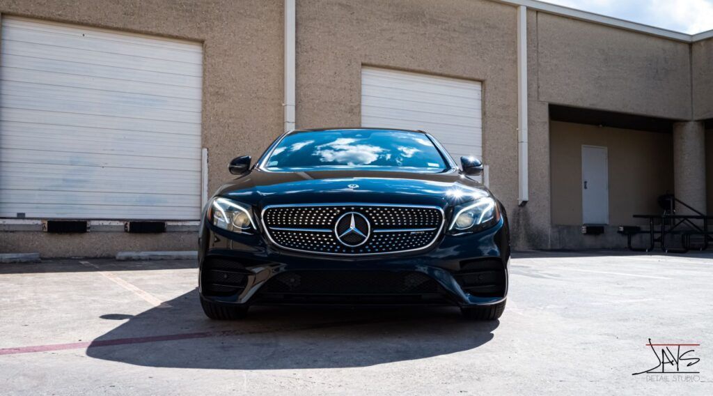 Black Mercedes-Benz sedan parked in front of a building with closed garage doors on a sunny day.