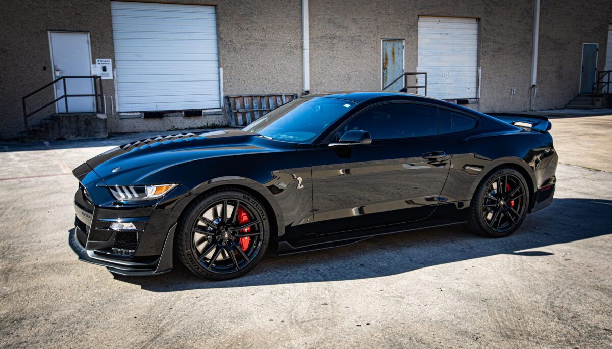 Black Ford Mustang sports car with red brake calipers parked outside a building.