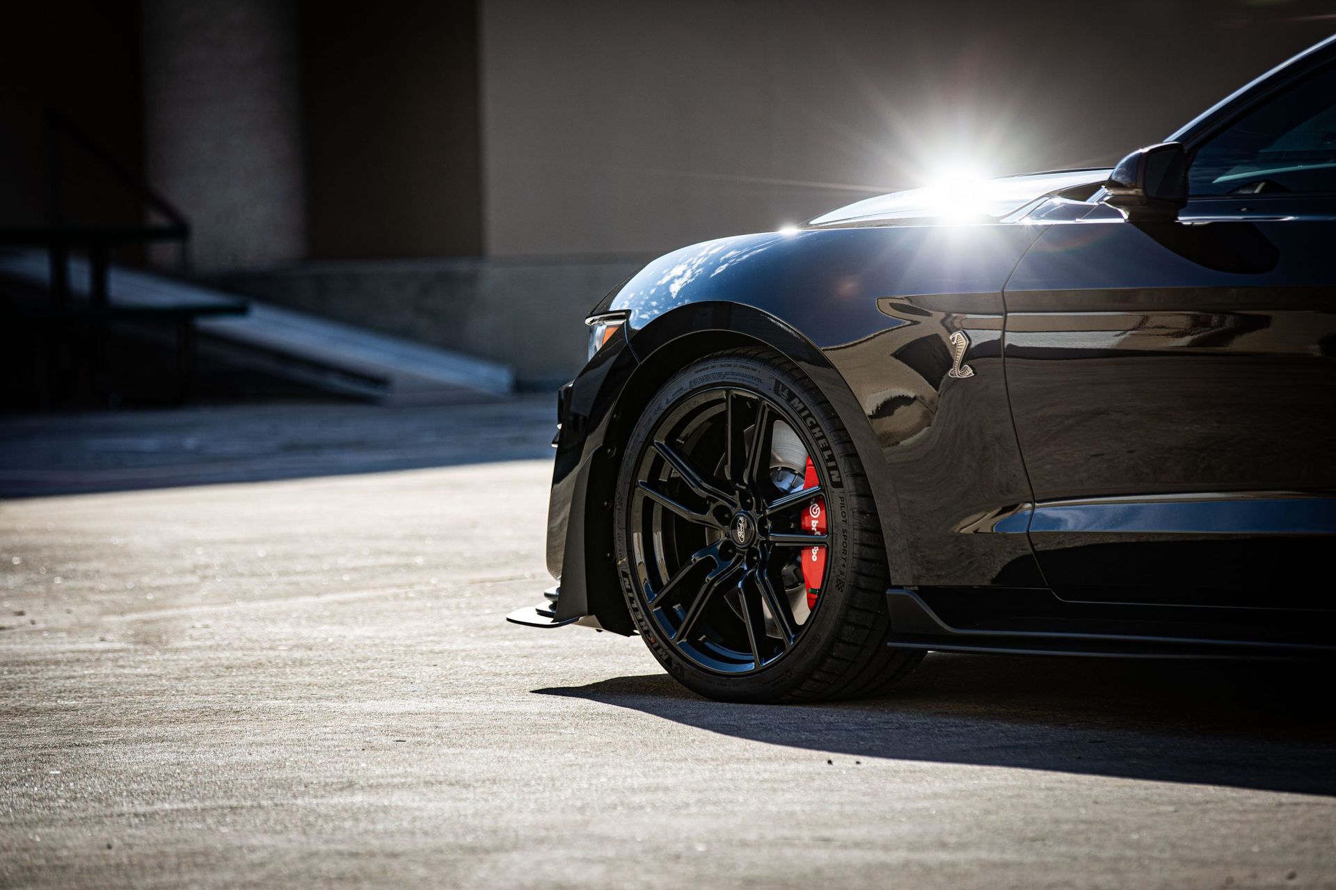 Black sports car, side view, bright sunlight, black wheels with red brake calipers, parked.