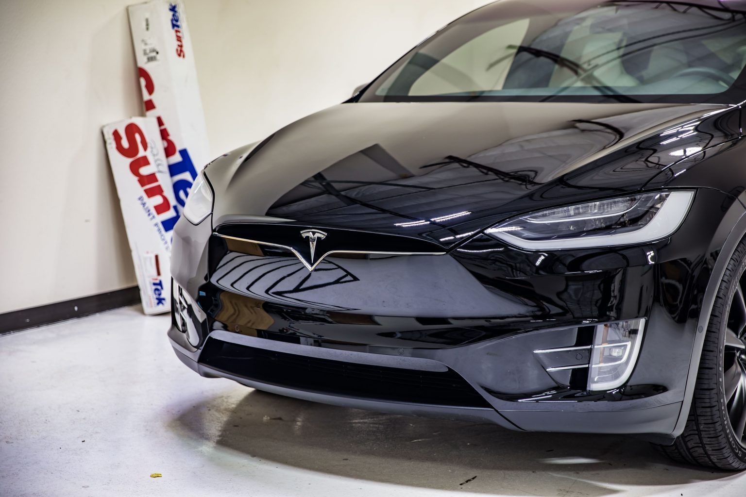 Black Tesla X car, parked indoors, near a sign.