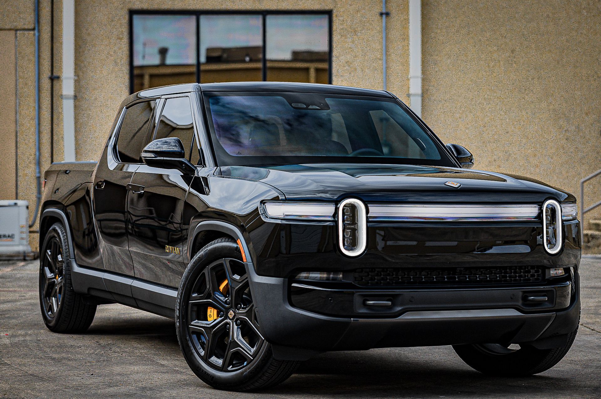 Black Rivian electric pickup truck parked in front of a building.