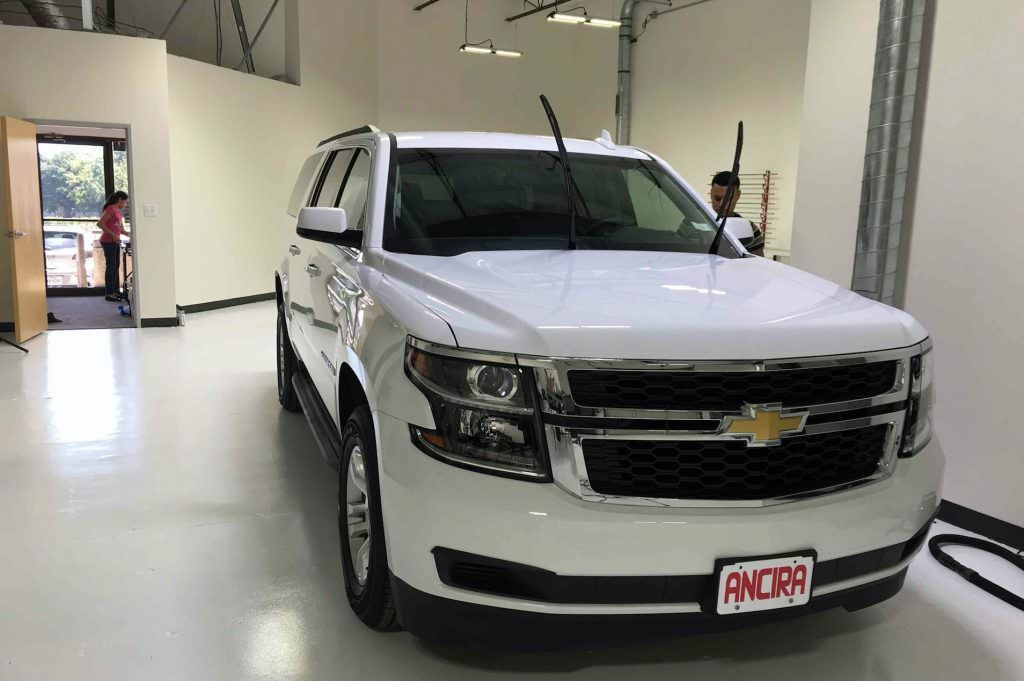 White SUV parked in a garage; two people are near the vehicle.