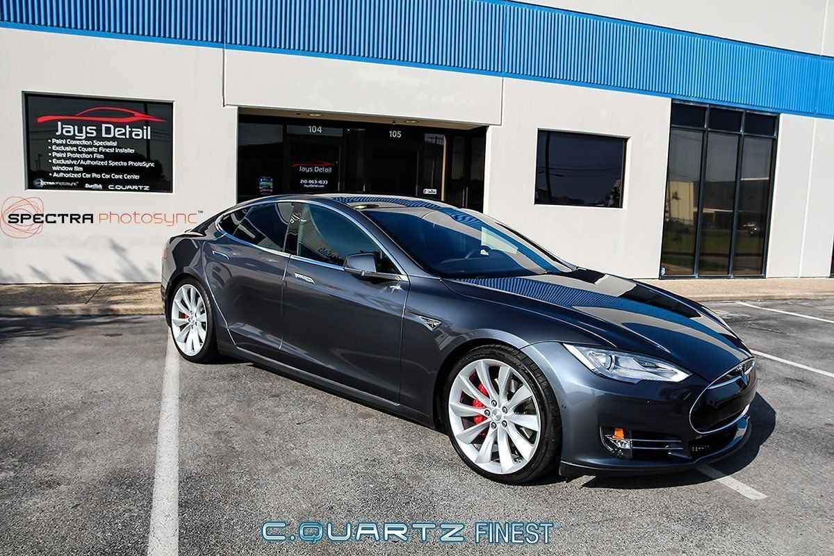 Gray Tesla parked in front of a building with red brake calipers and silver rims.