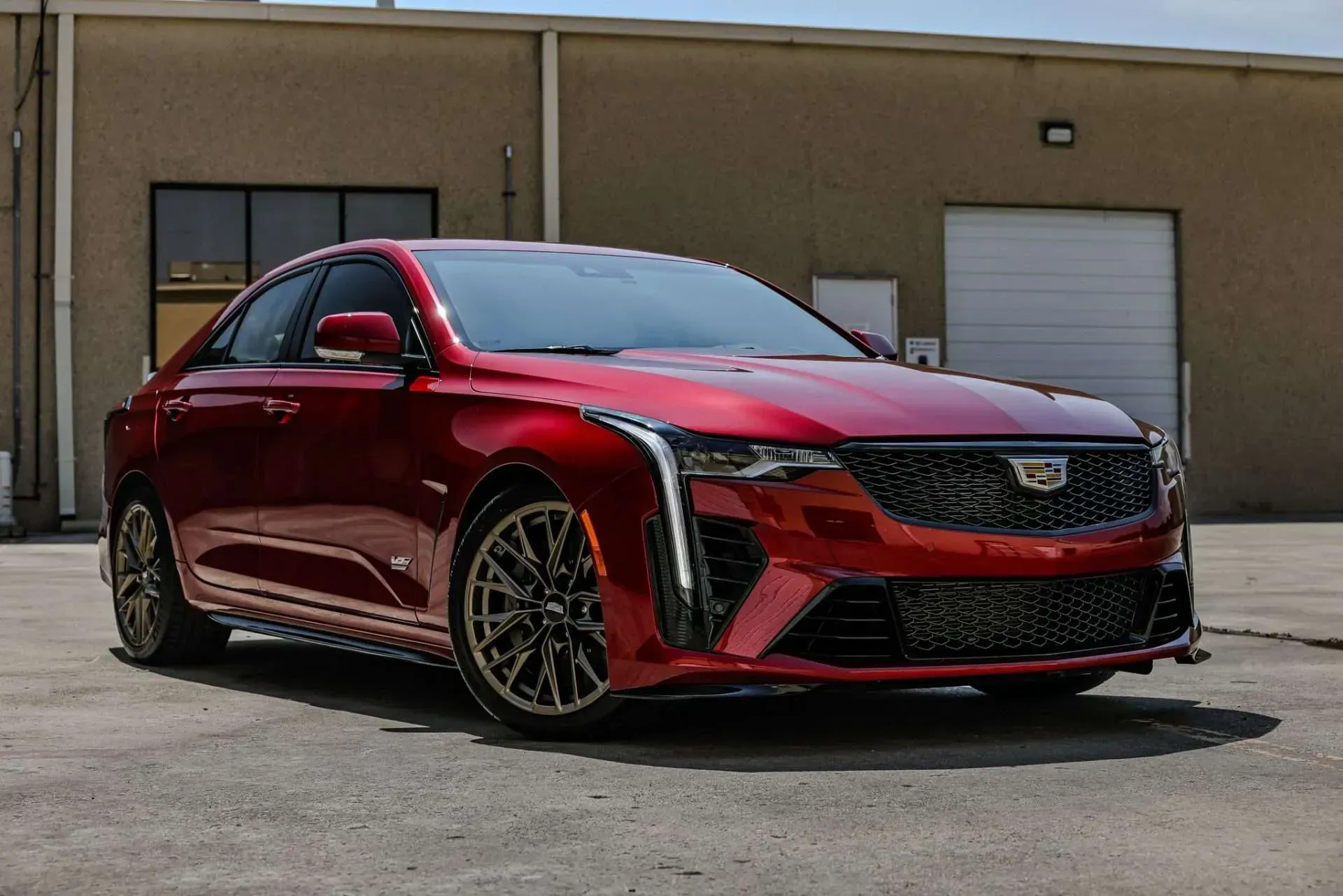 Red Cadillac CT4-V sedan parked in front of a tan industrial building.