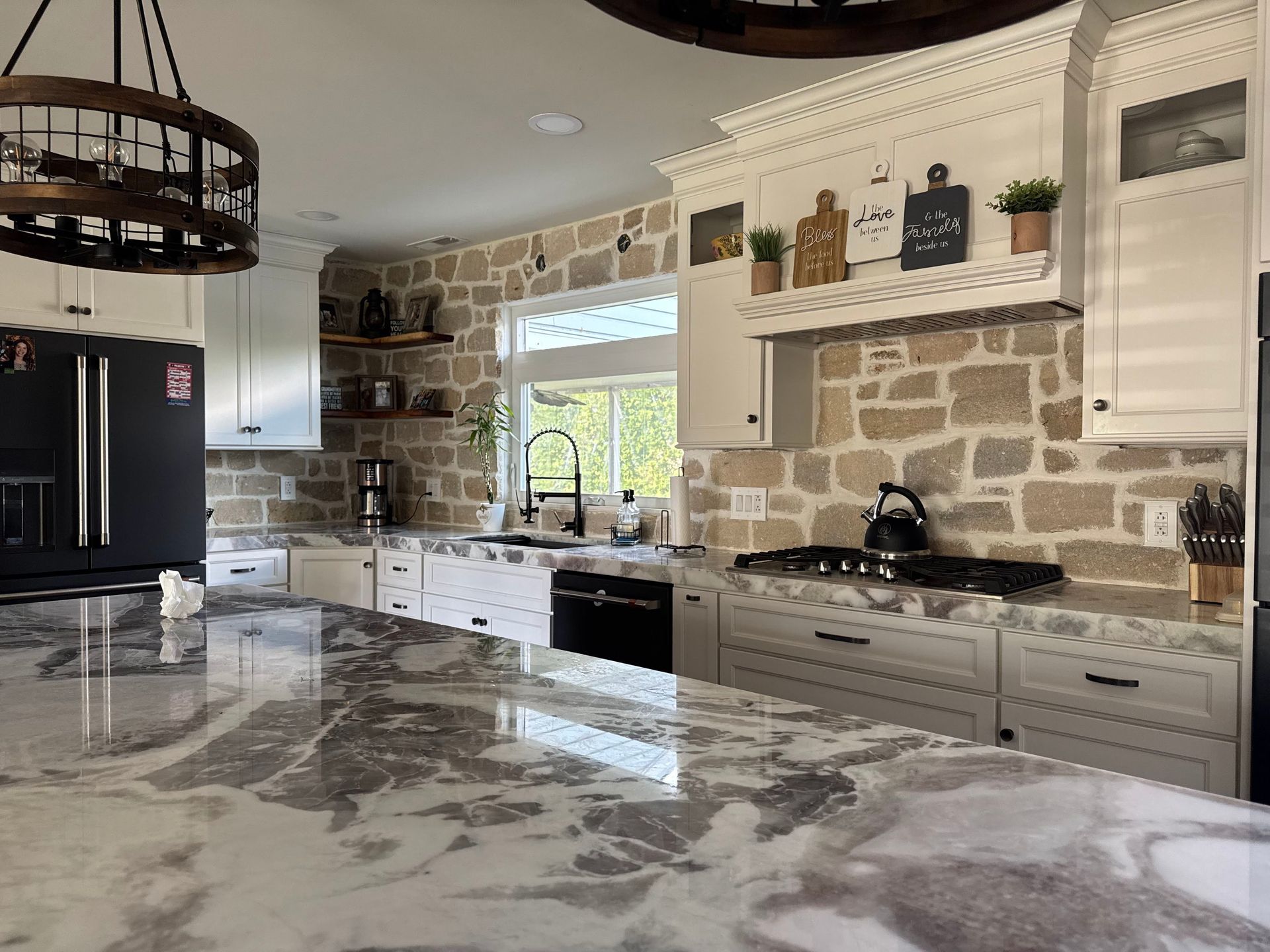 A kitchen with white cabinets , granite counter tops , and a black refrigerator.
