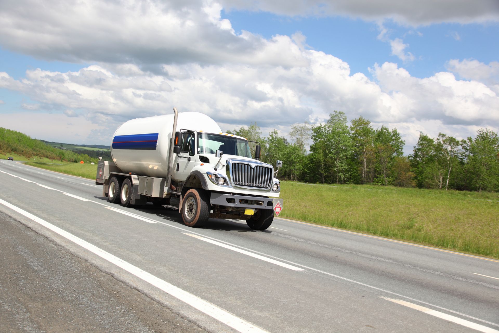 A white propane delivery truck driving on a highway to make a scheduled customer delivery.