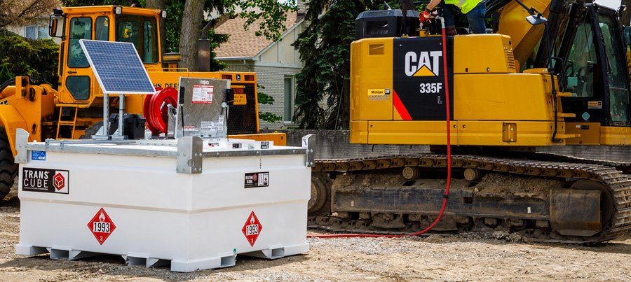 A yellow CAT excavator is being fueled from a white fuel tank on a construction site.