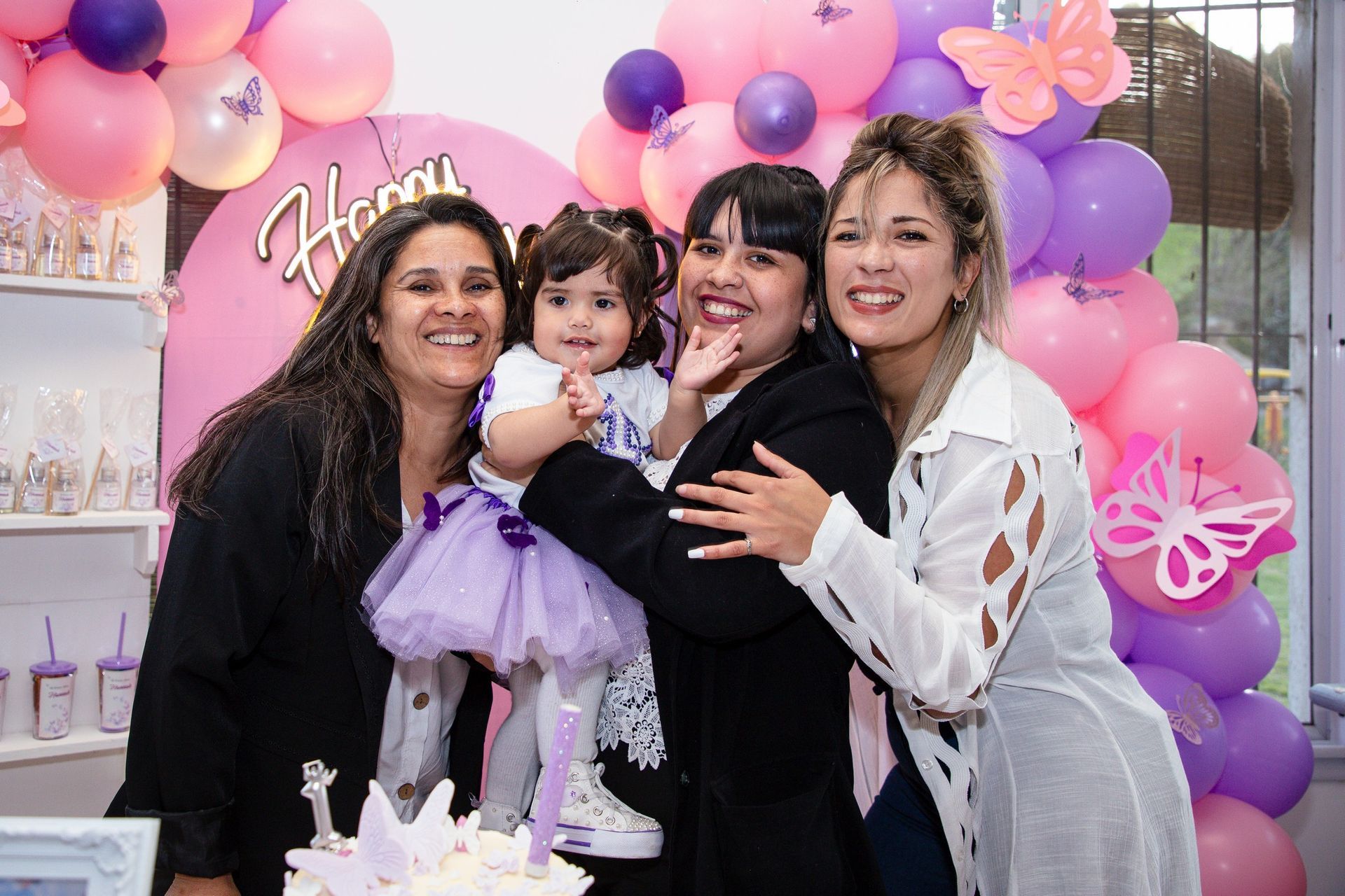 Cuatro personas sonríen a la cámara. Una niña con tutú es sostenida por una mujer con globos al fondo.