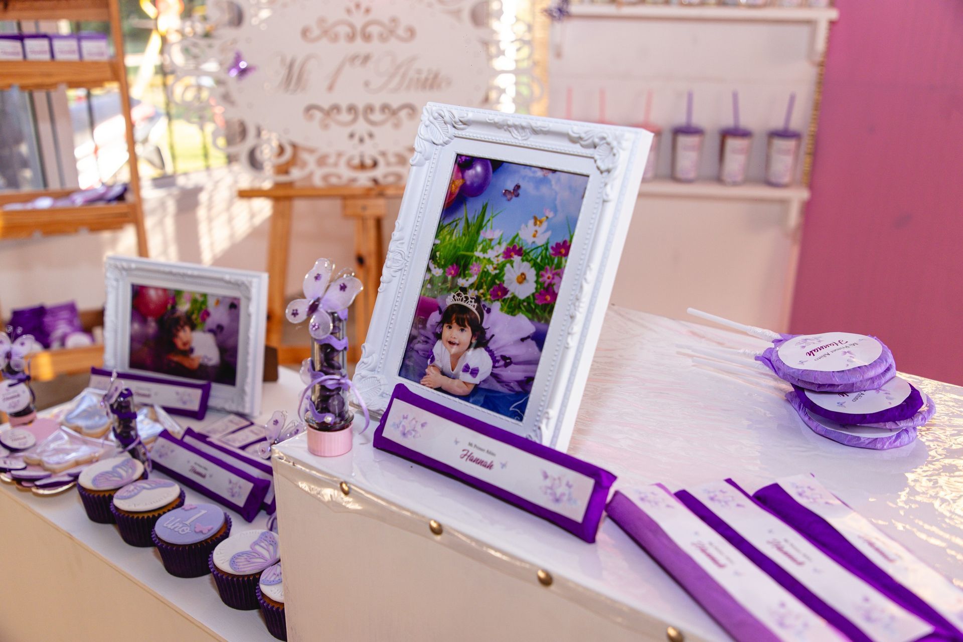 Una mesa de fiesta con fotografías enmarcadas, cupcakes y decoraciones moradas.