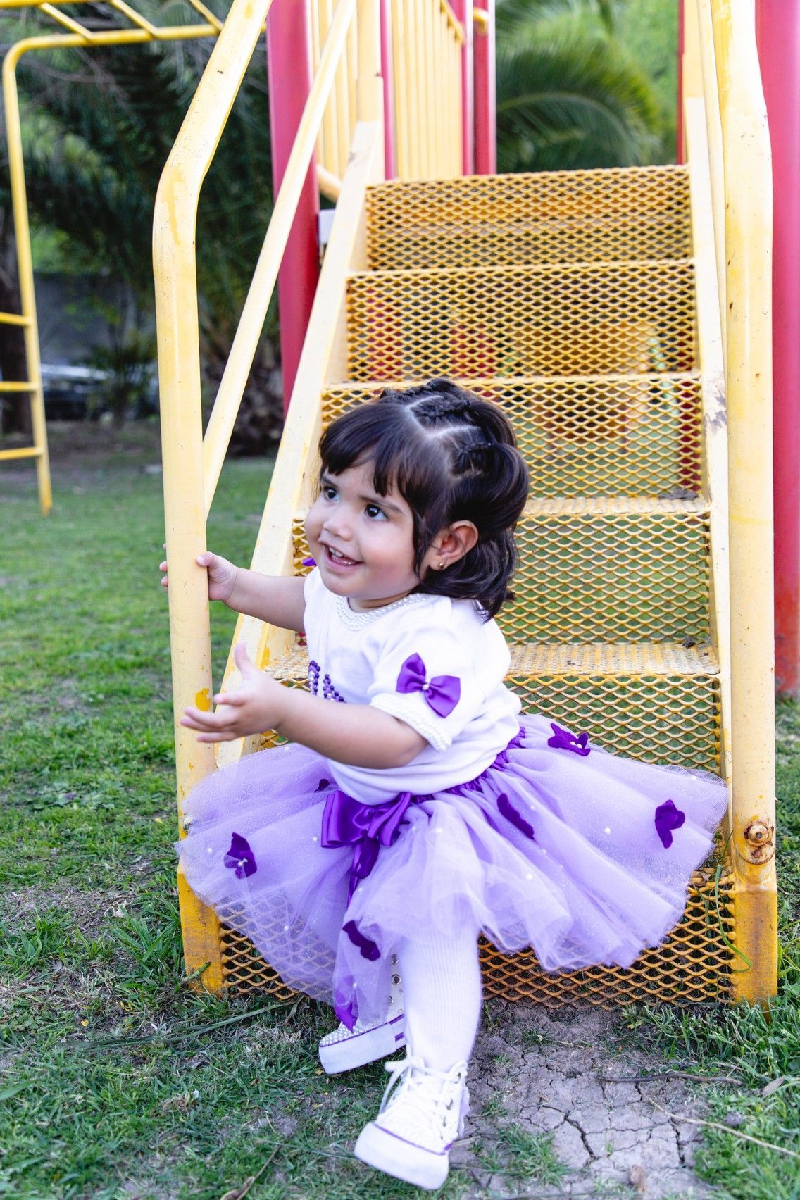 Una niña con un tutú morado sonríe en los escalones amarillos del patio de recreo.