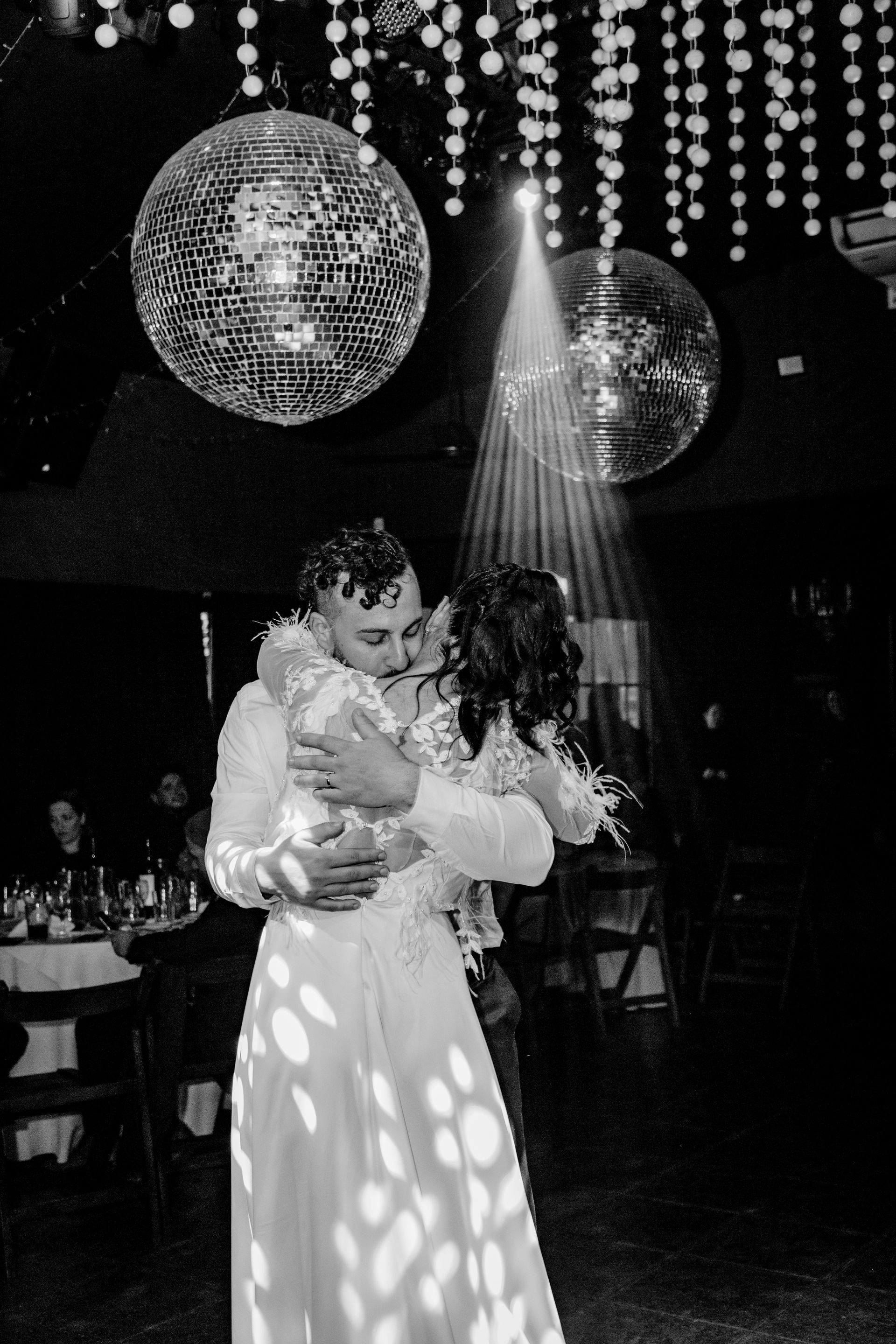 Recién casados bailando bajo bolas de discoteca, abrazados y con luces deslizándose hacia abajo.