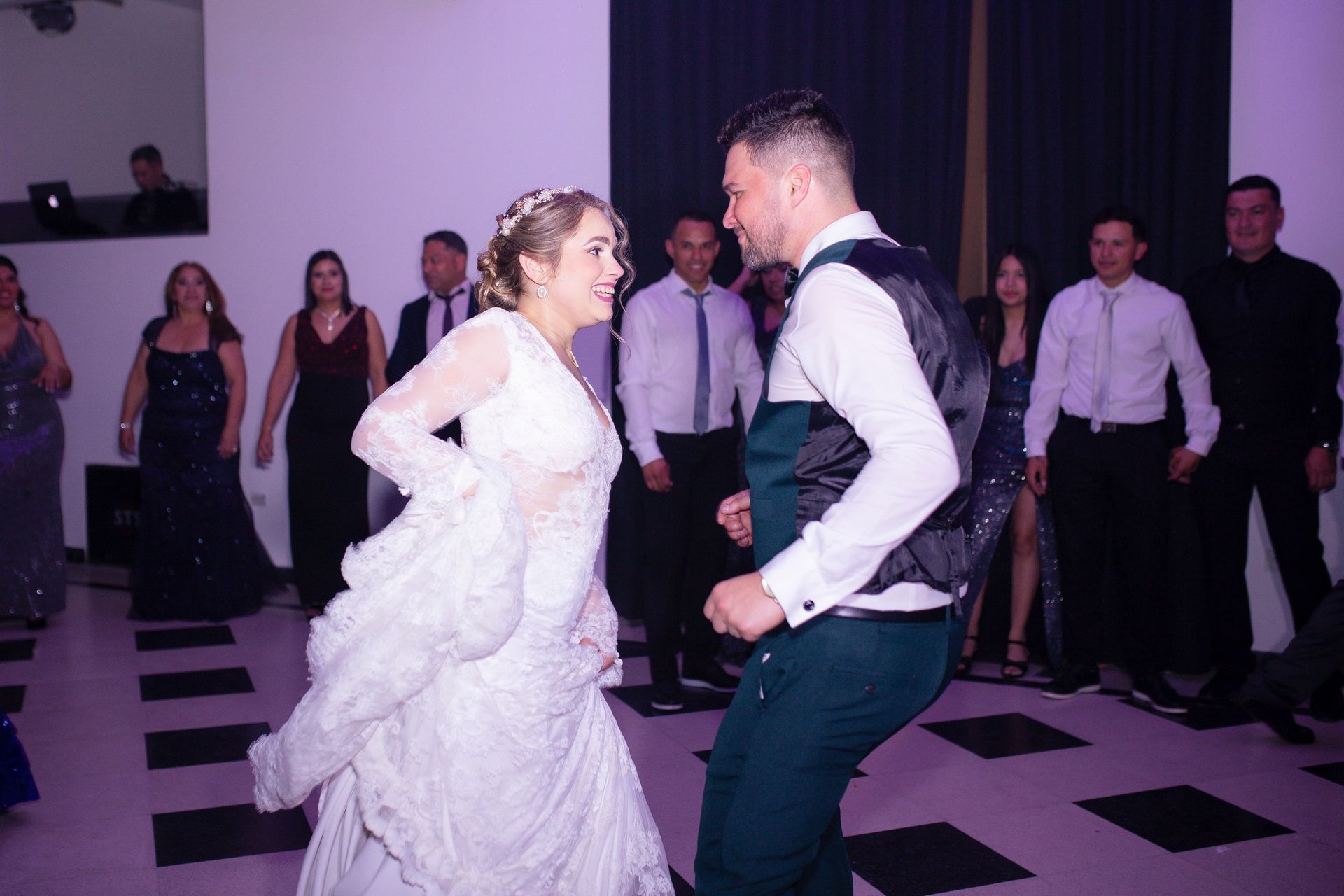 Novios bailando en una recepción de boda. Los invitados observan, la sala iluminada con luz violeta.