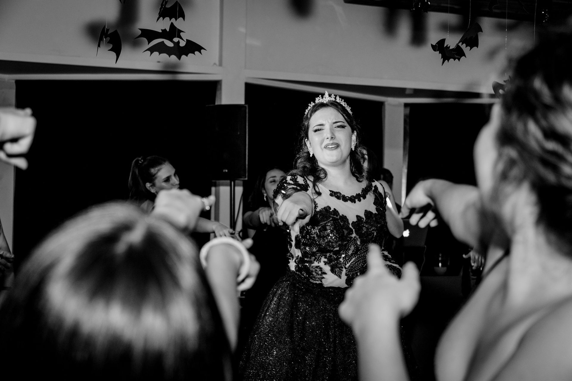 Mujer vestida de gala y con tiara baila con amigas, con los brazos en alto, en una fiesta.