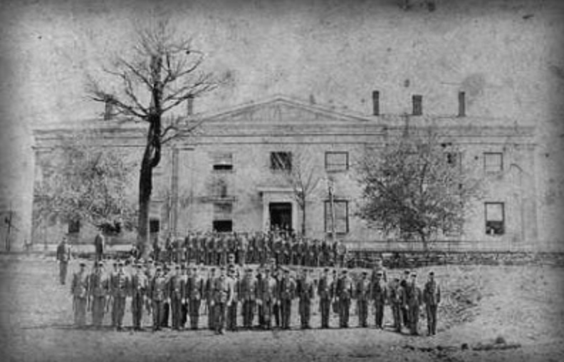 A black and white photo of a group of people standing in front of a large building.