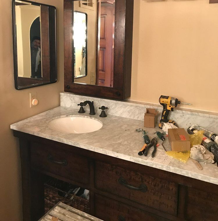 Bathroom vanity with dark wood cabinets, white marble countertop, and tools.