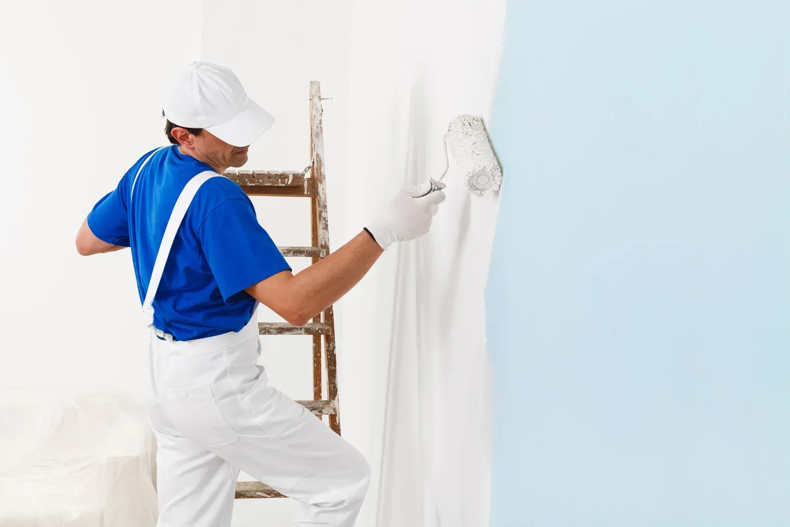 A man is standing on a ladder painting a wall.