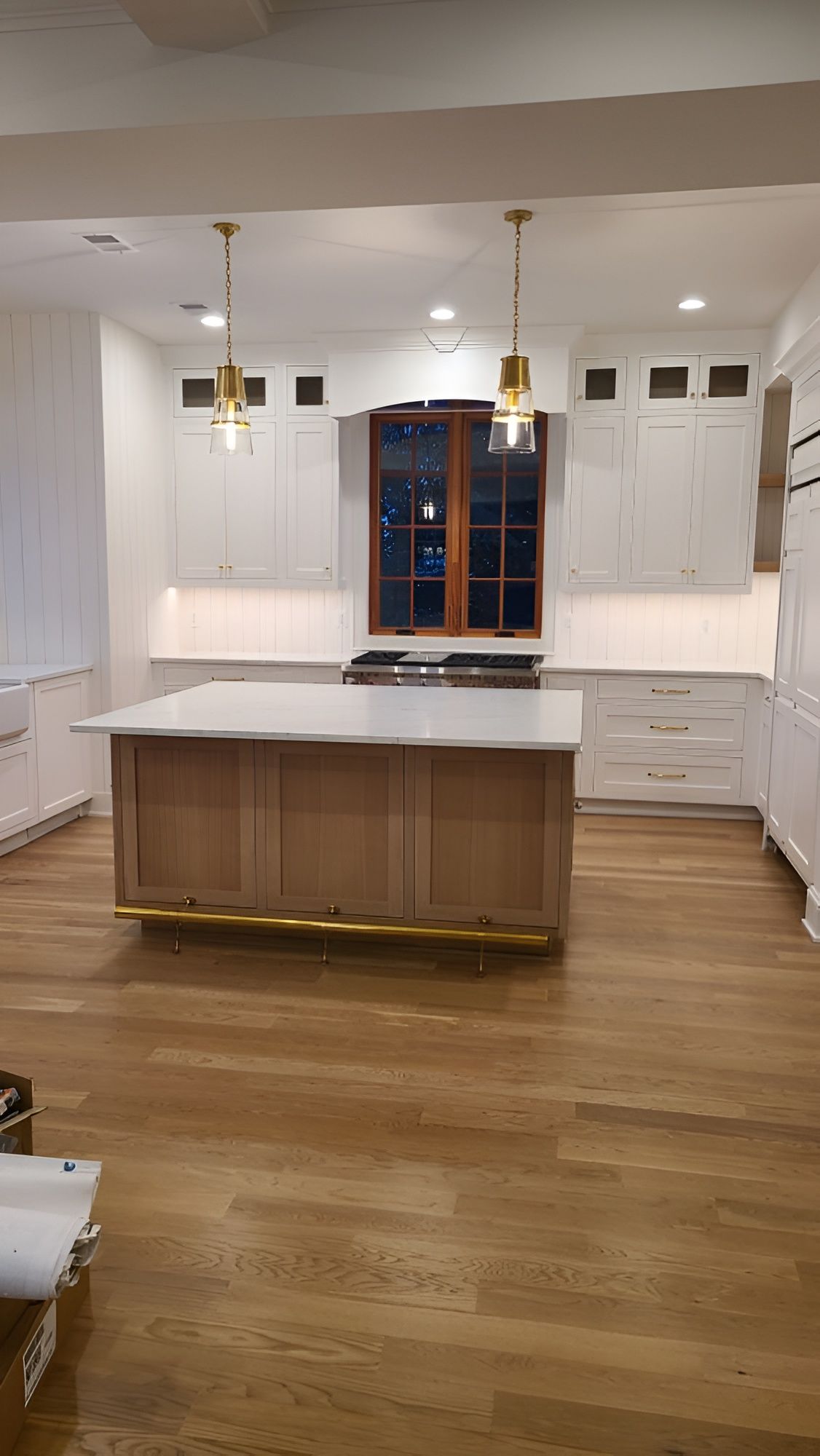 A modern kitchen with white cabinets, light wood island, and gold pendant lights.