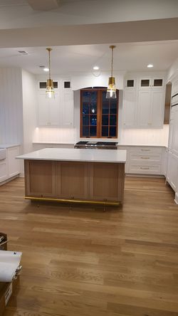 A modern kitchen with white cabinets, light wood island, and gold pendant lights.