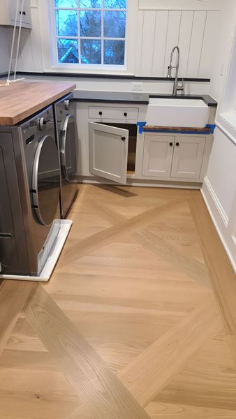 Laundry room with wooden chevron floor, washer/dryer, sink, and cabinets.