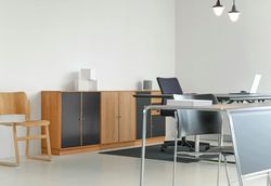Modern office space with desk, cabinets, chairs, and laptop against a white wall.