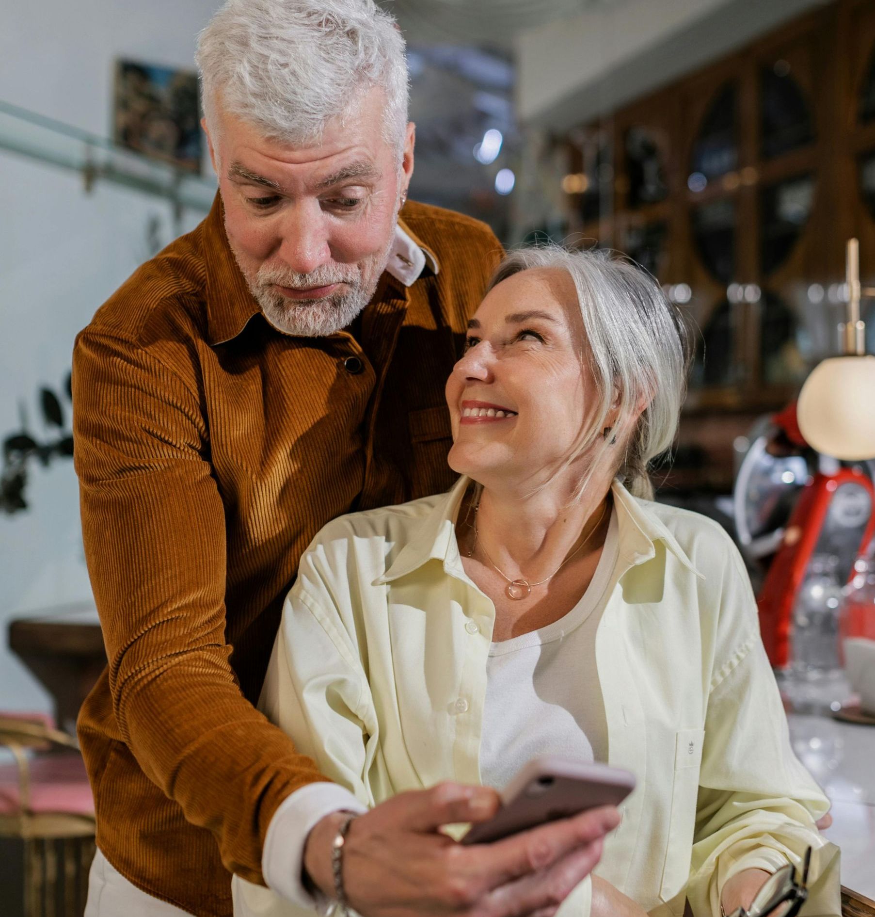 An older woman and man are smiling and looking at a cell phone together.
