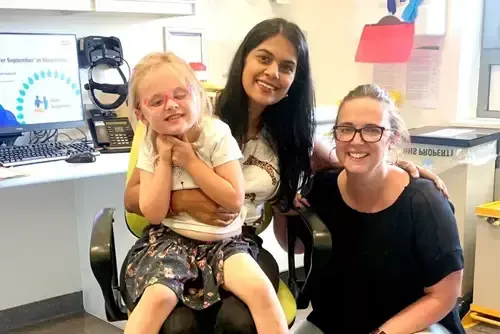 A little girl is sitting in a dental chair with two women.