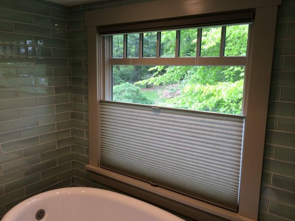 Cellular shades, light gray in color, are installed in a top-down, bottom-up style on a window above a white bathtub. 
