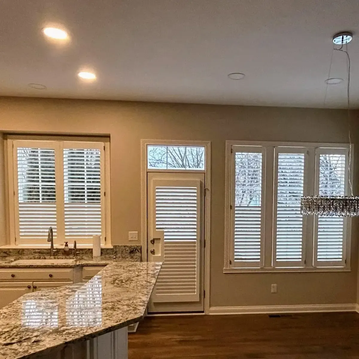 A bright, spacious kitchen with a breakfast bar and hardwood floors, featuring premium plantation shutters on the windows and back door.