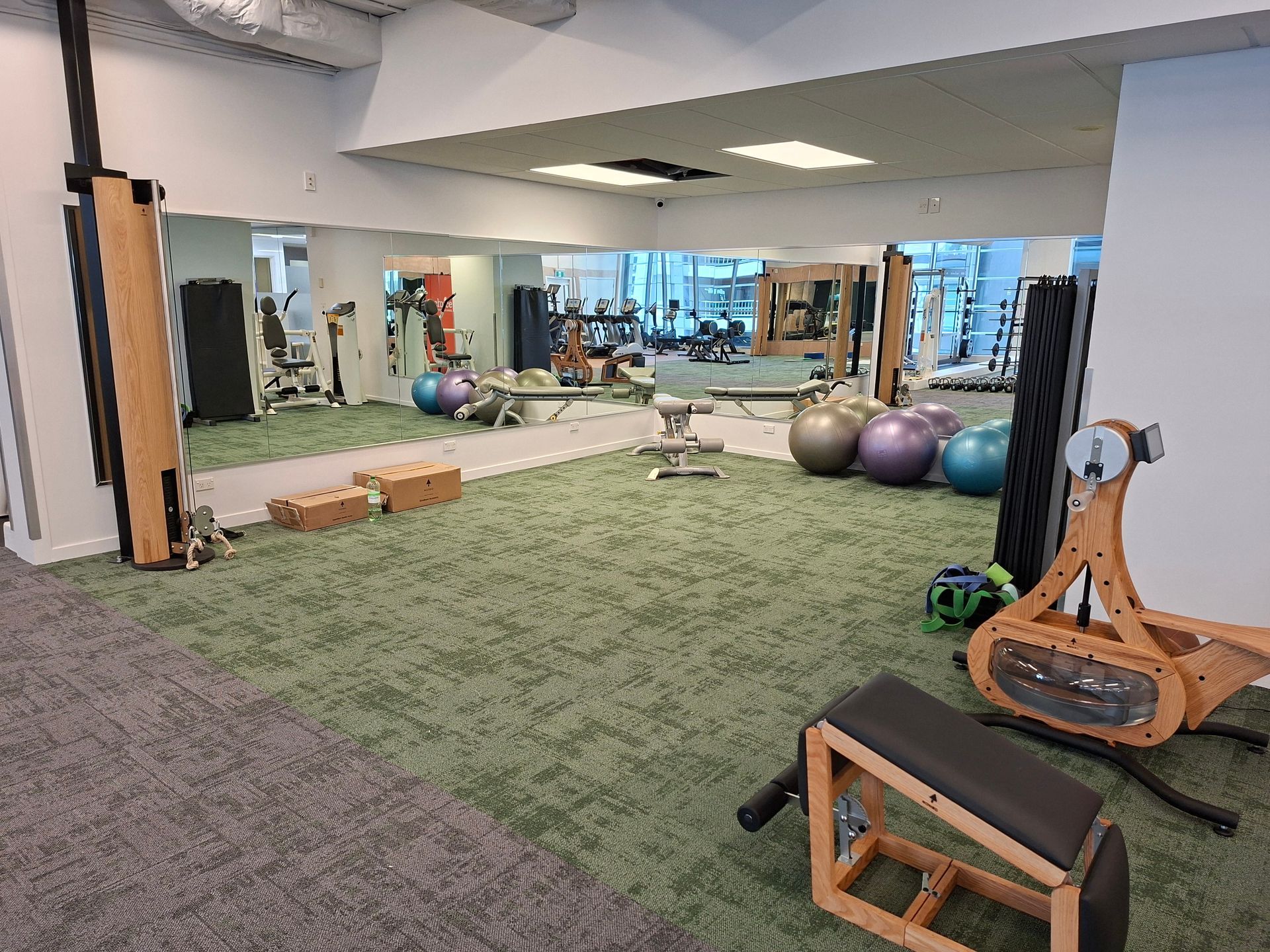 A modern gym with weight machines, benches, and free weights. Brown carpet and white walls.