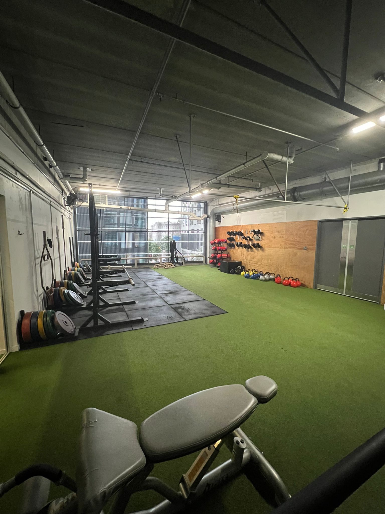 A fitness studio with weight racks, turf flooring, and equipment; a person is in the background.