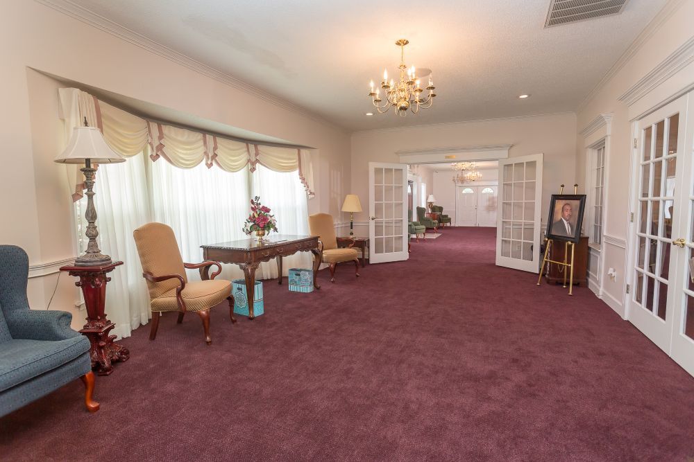 A living room with a purple carpet , chairs , a table and a chandelier.