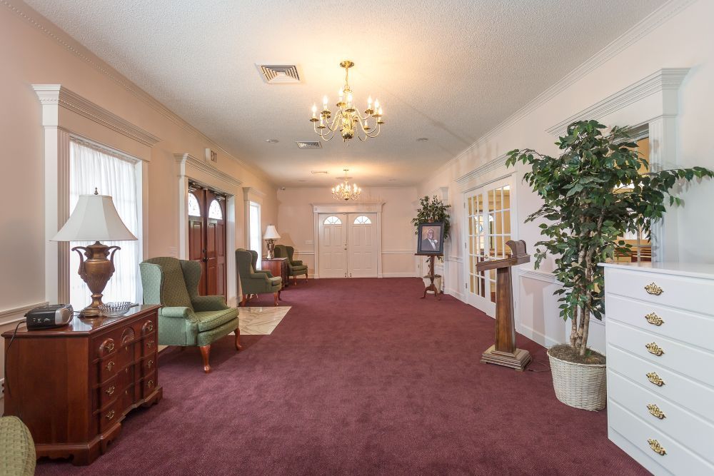 A long hallway with a red carpet and chairs in a funeral home.