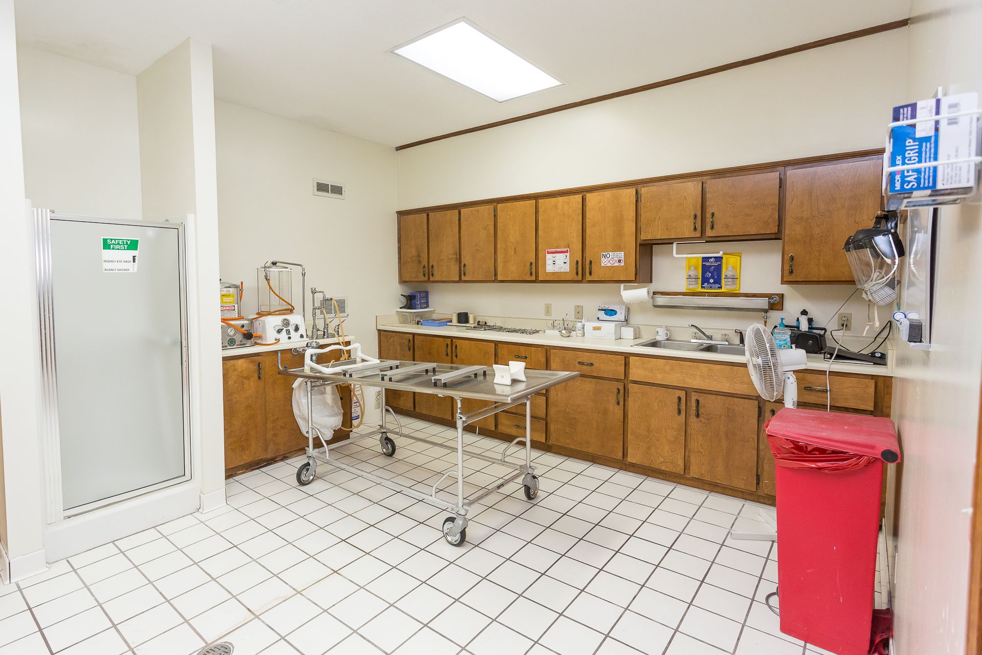 A kitchen with wooden cabinets , a metal table and a red trash can.
