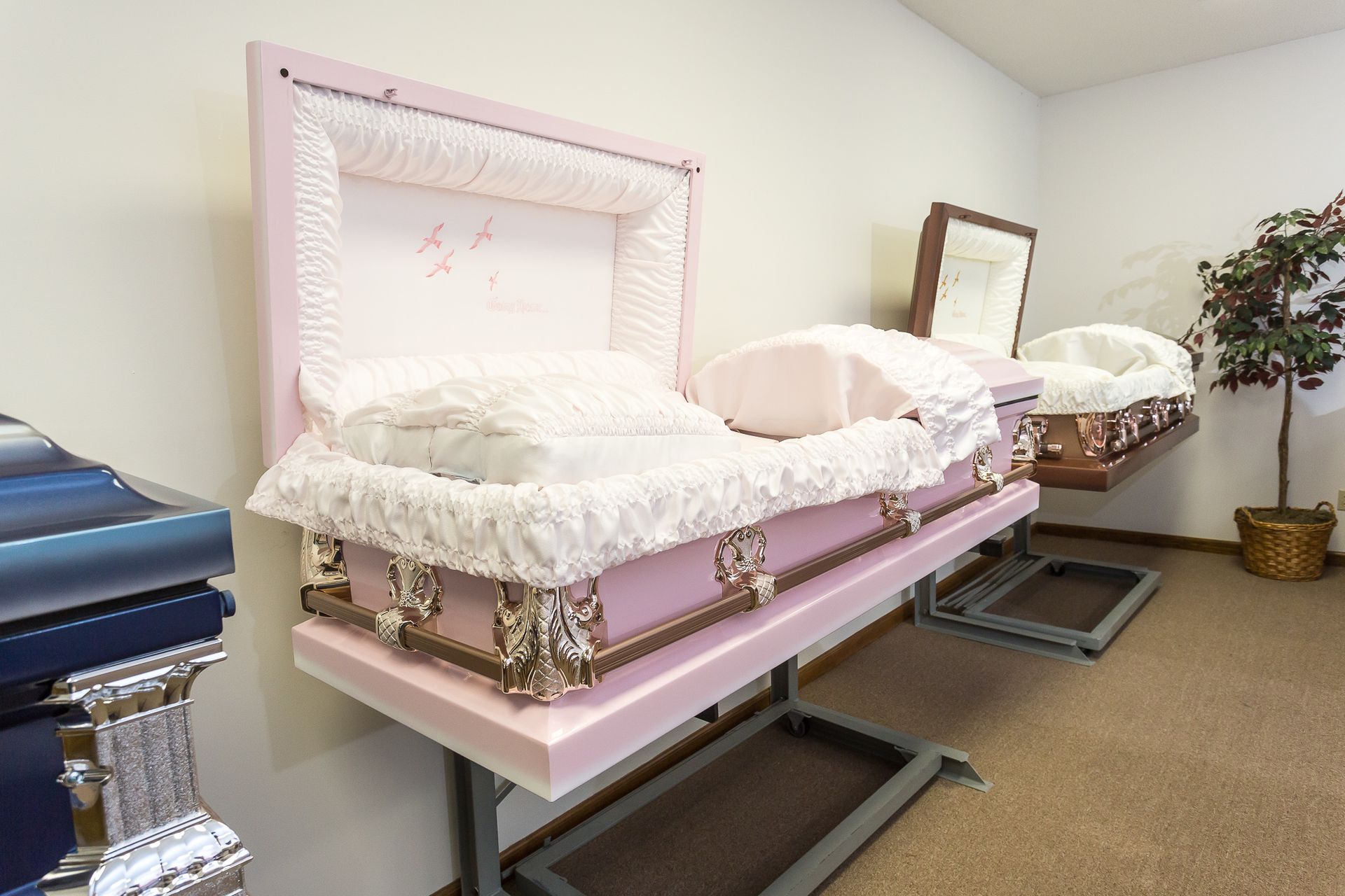 A pink coffin is sitting on a stand in a room with other coffins.