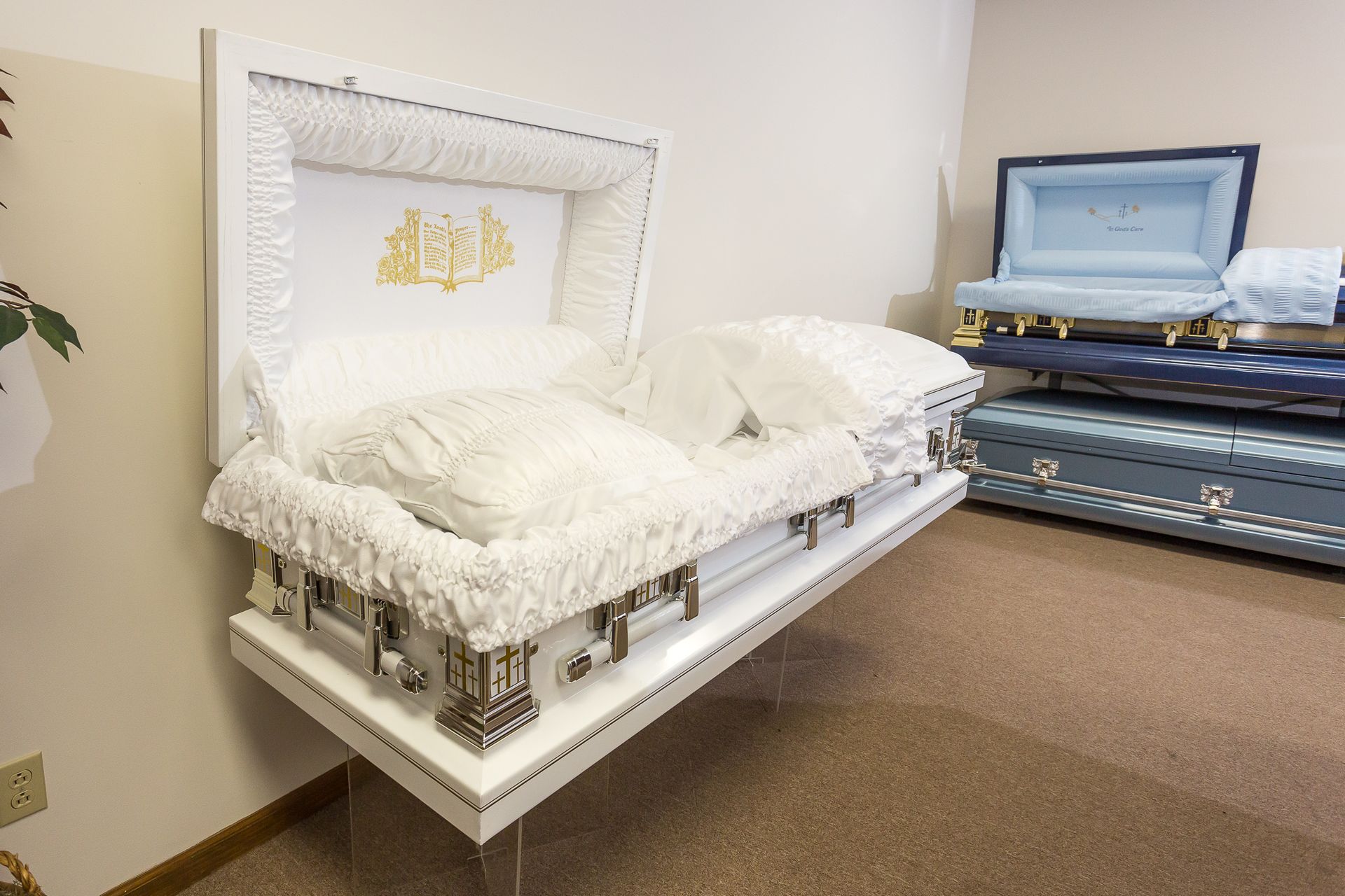A white coffin is sitting in a room next to a stack of blue coffins.