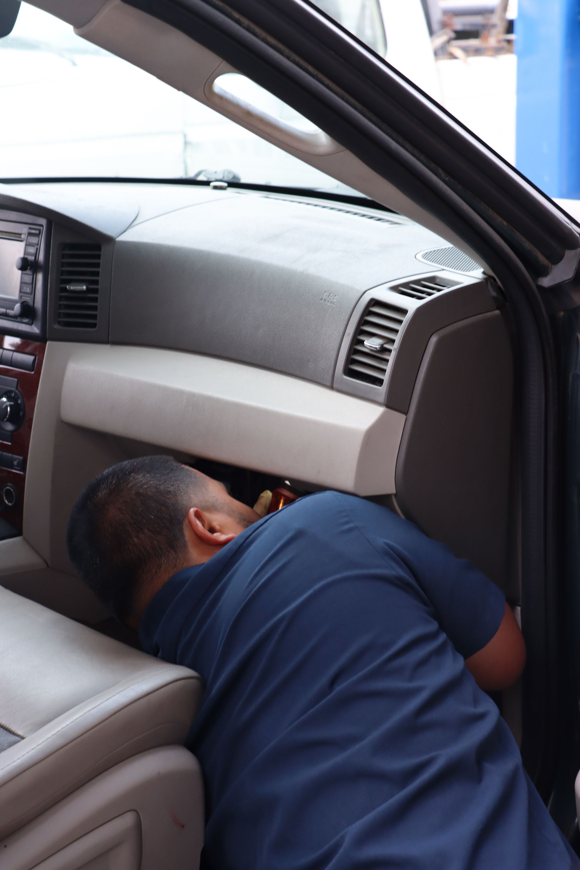 A man in a blue shirt is working on the dashboard of a car