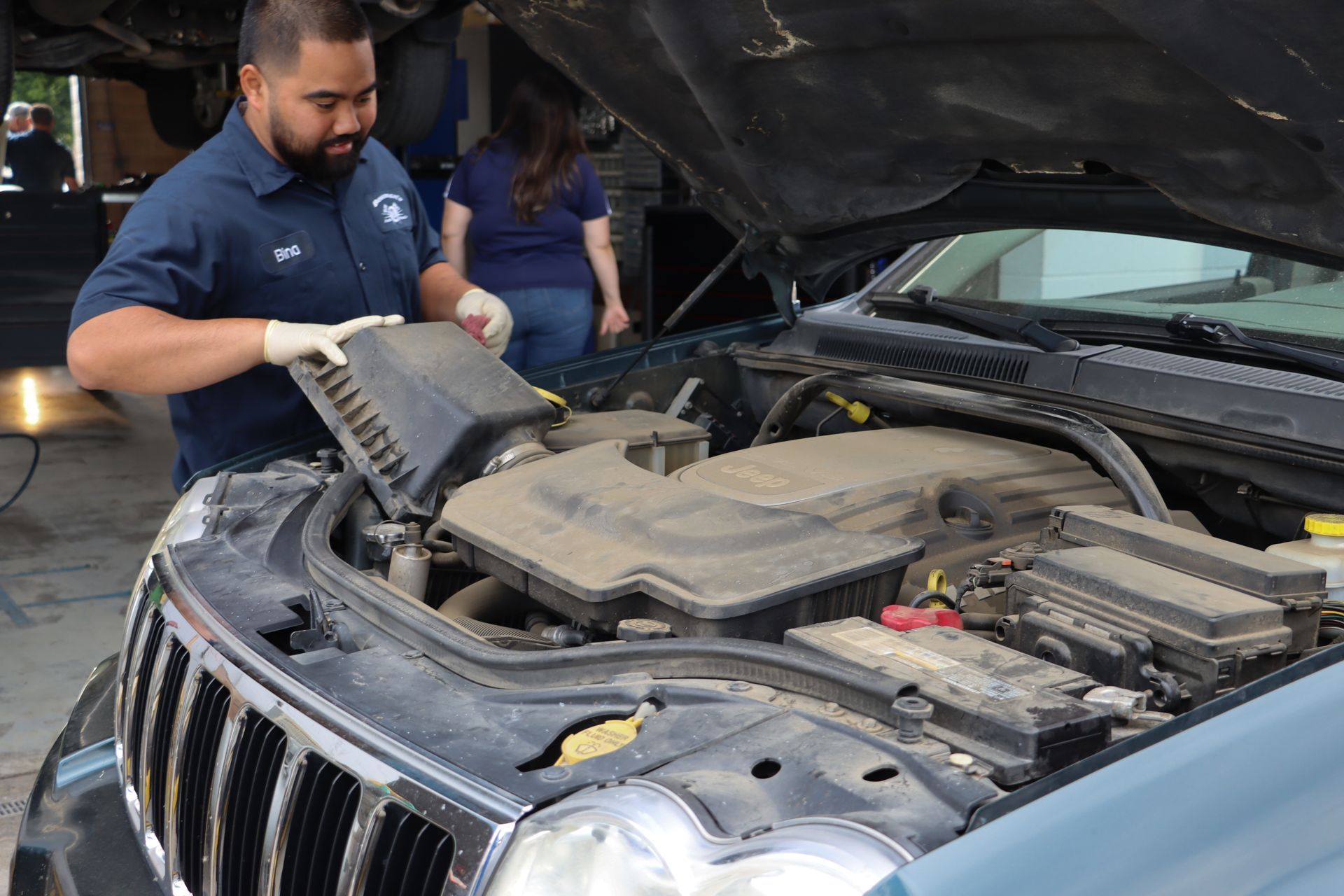 A man is looking under the hood of a jeep.