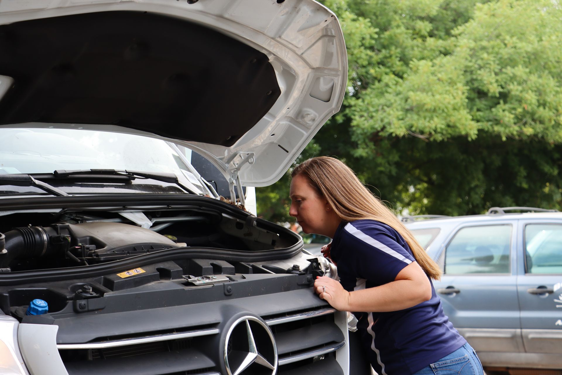 A woman is looking under the hood of a mercedes