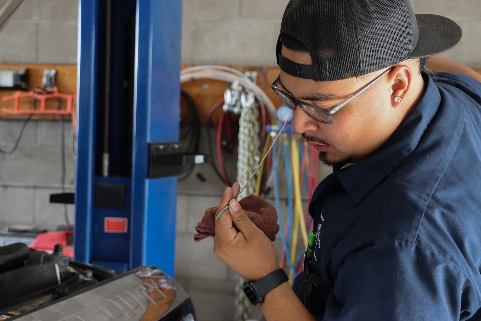 A man wearing a hat and glasses is working on a machine in a garage.