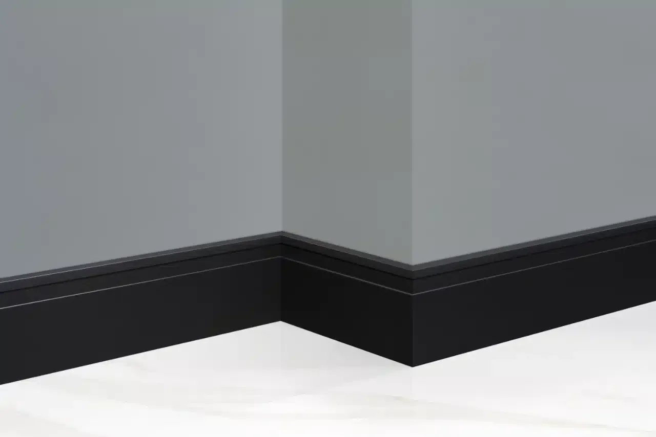 Un rincón de una habitación con un rodapié negro y una pared gris.