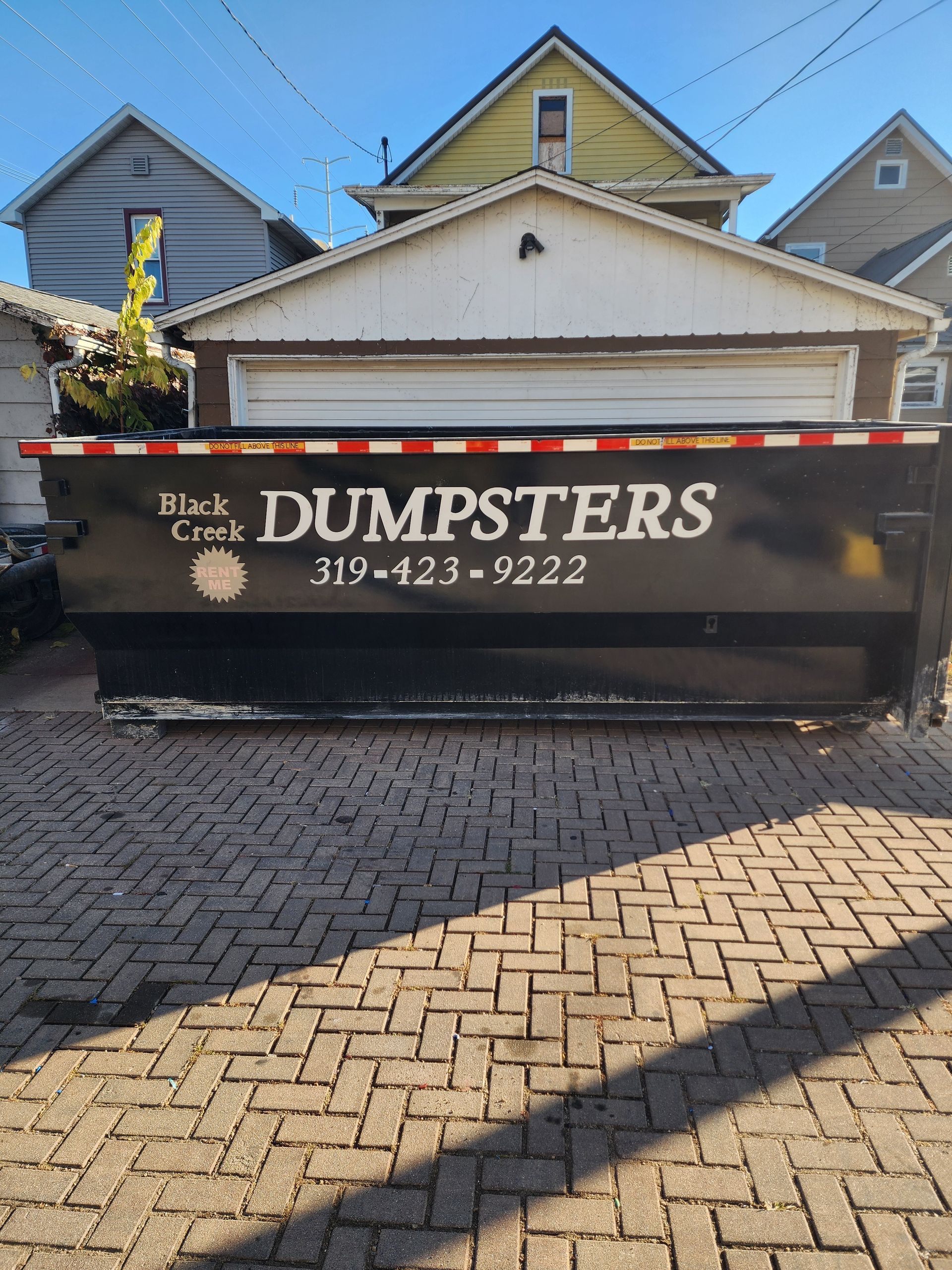 Black dumpster from Black Creek Dumpsters with a garage background.