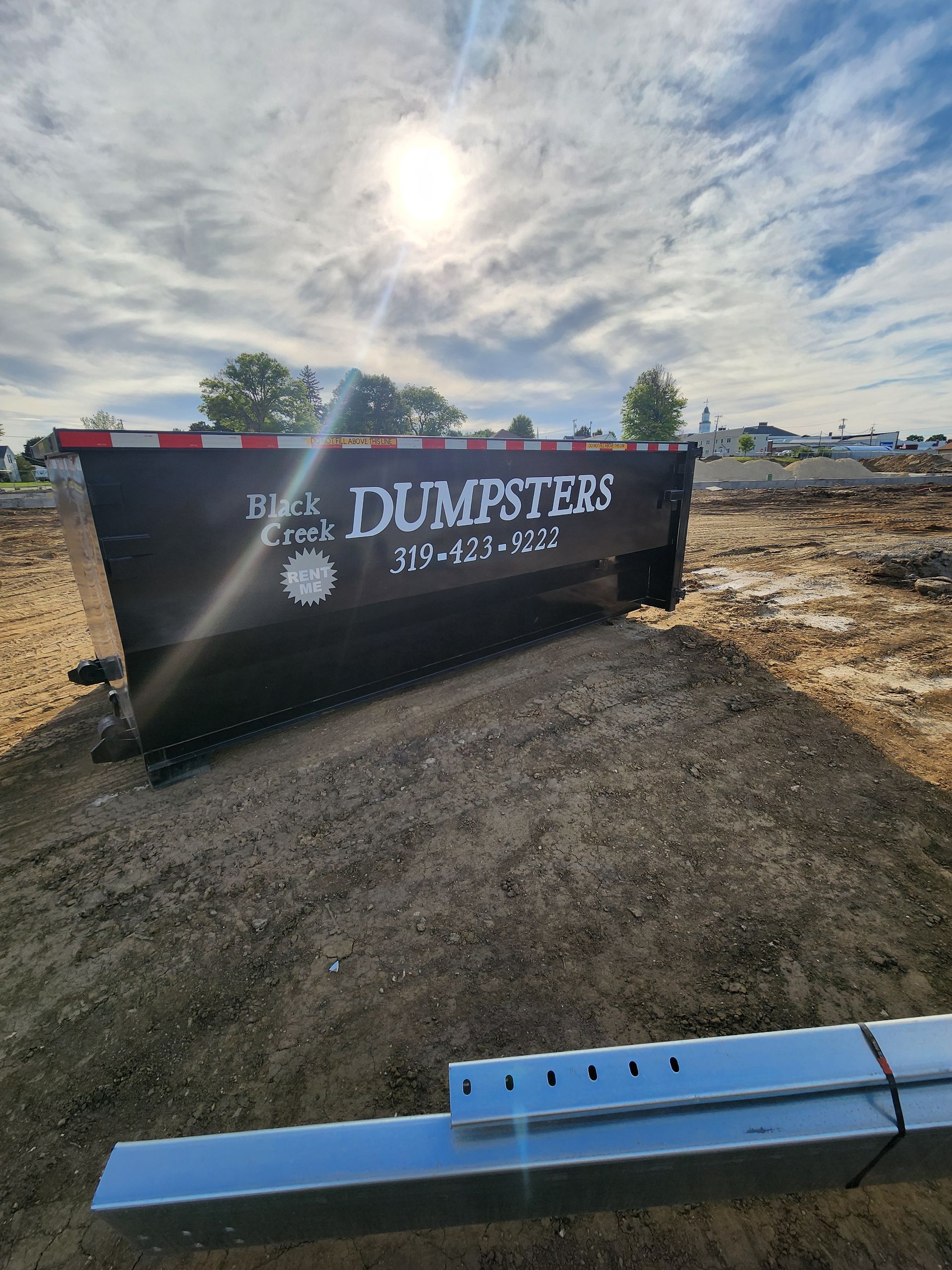 Black dumpster with on a gravel pile, sunny sky.