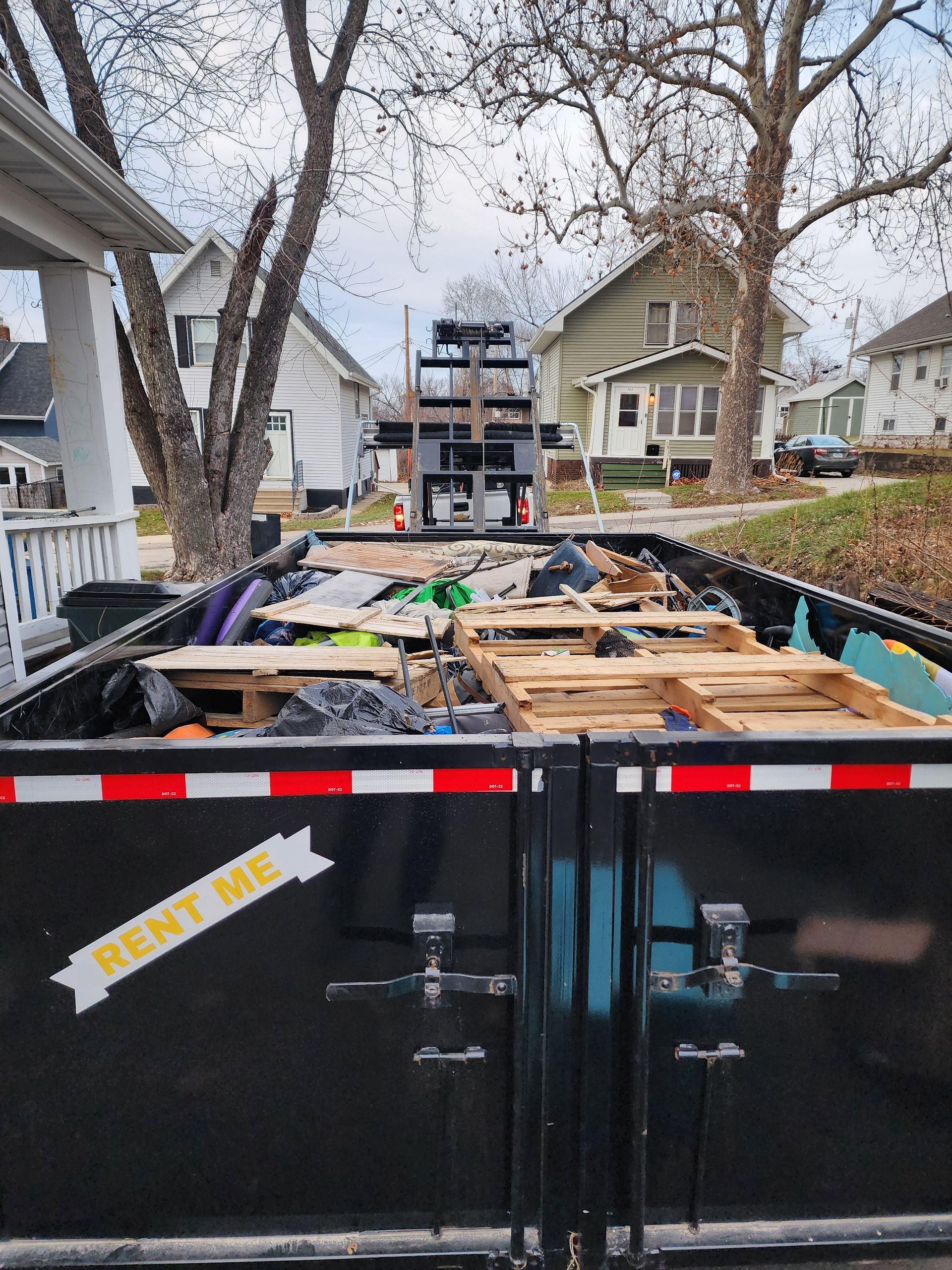 Black dumpster filled with debris, pallets, and trash in a residential area.