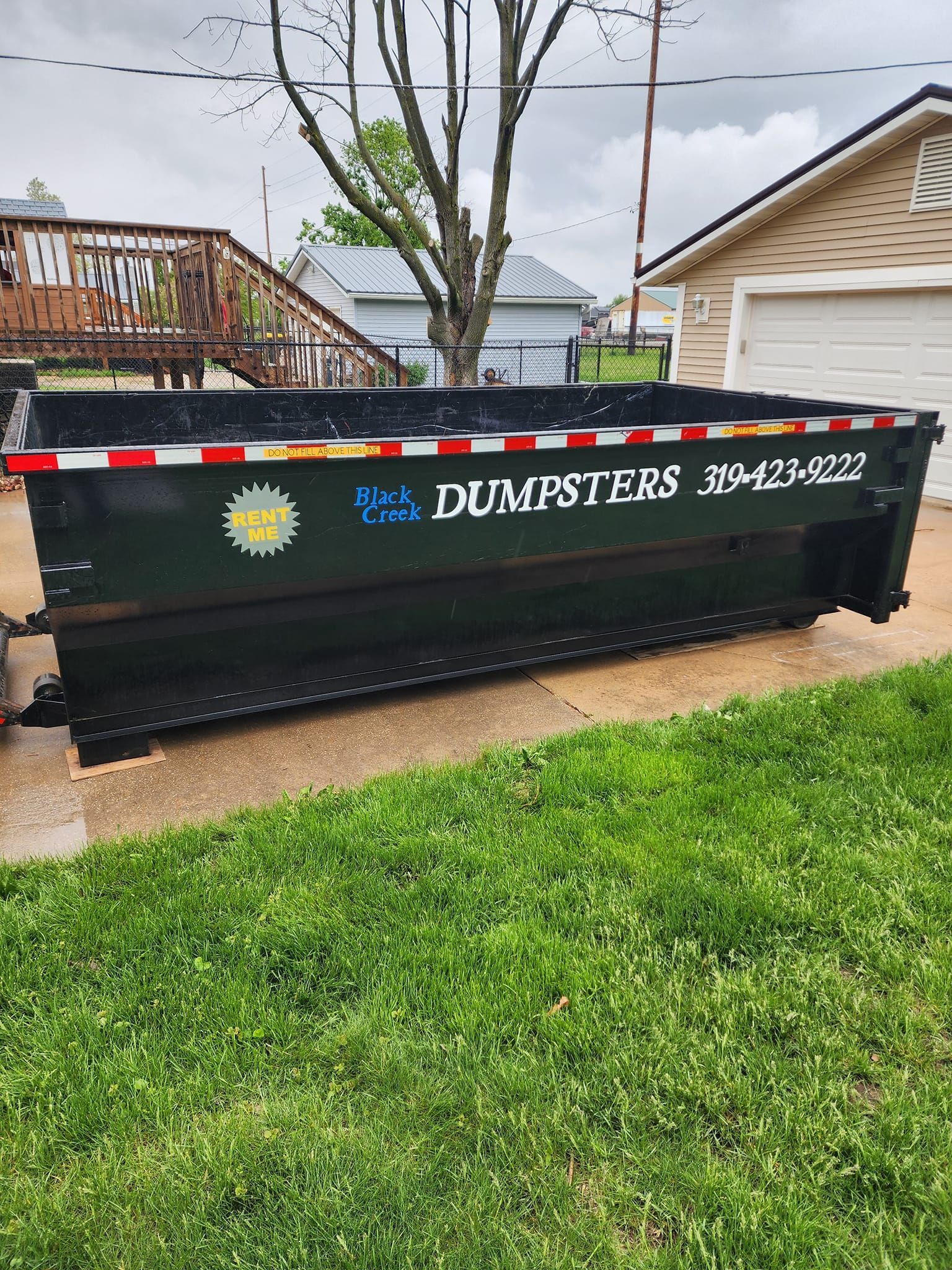 Black dumpster on grass with phone number on the side.