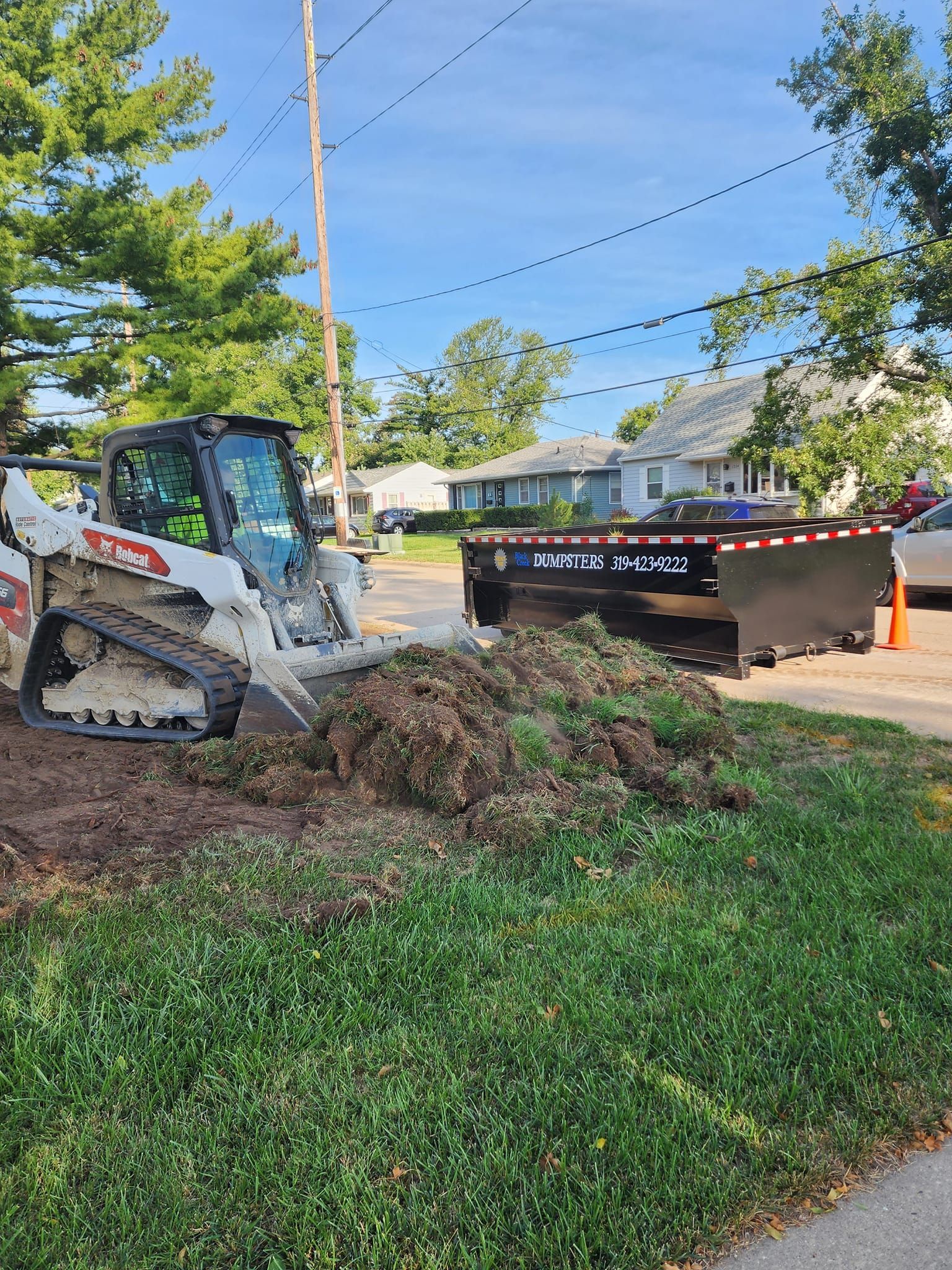 Bobcat skid-steer loading debris into a trailer on a residential street.