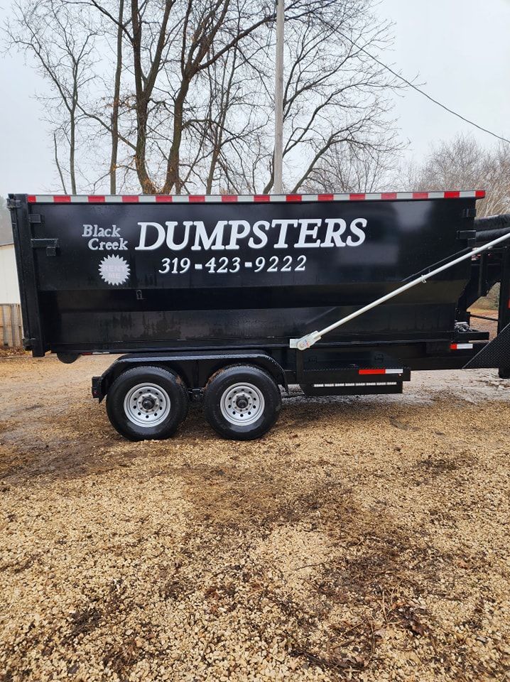 Black dumpster trailer with phone number on a gravel surface.