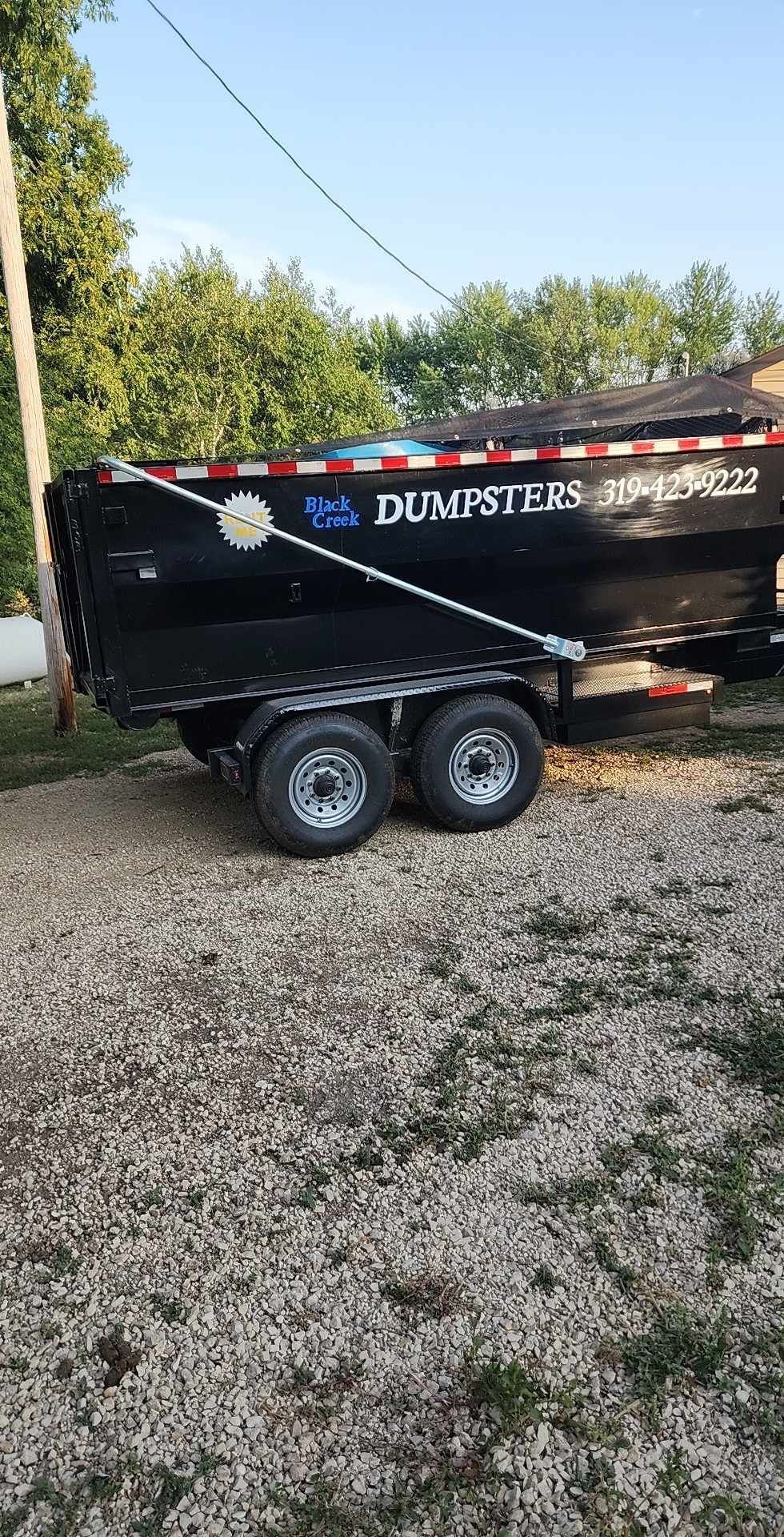 Black dumpster trailer parked on gravel.