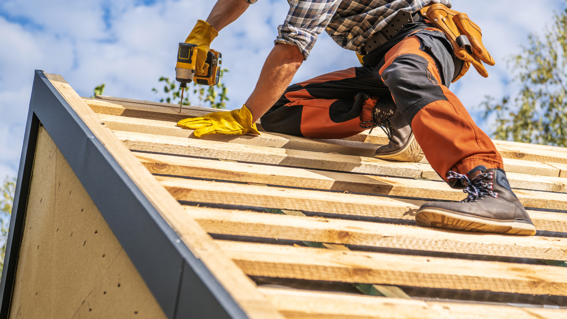 A man wearing a hard hat and gloves is working on a roof.