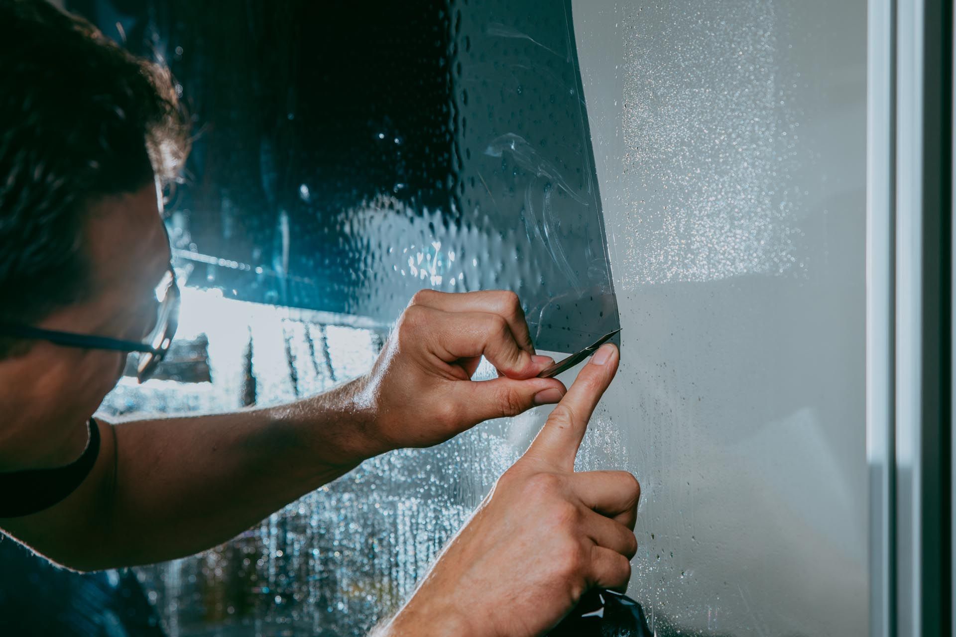 A man is applying tinted glass to a car window.