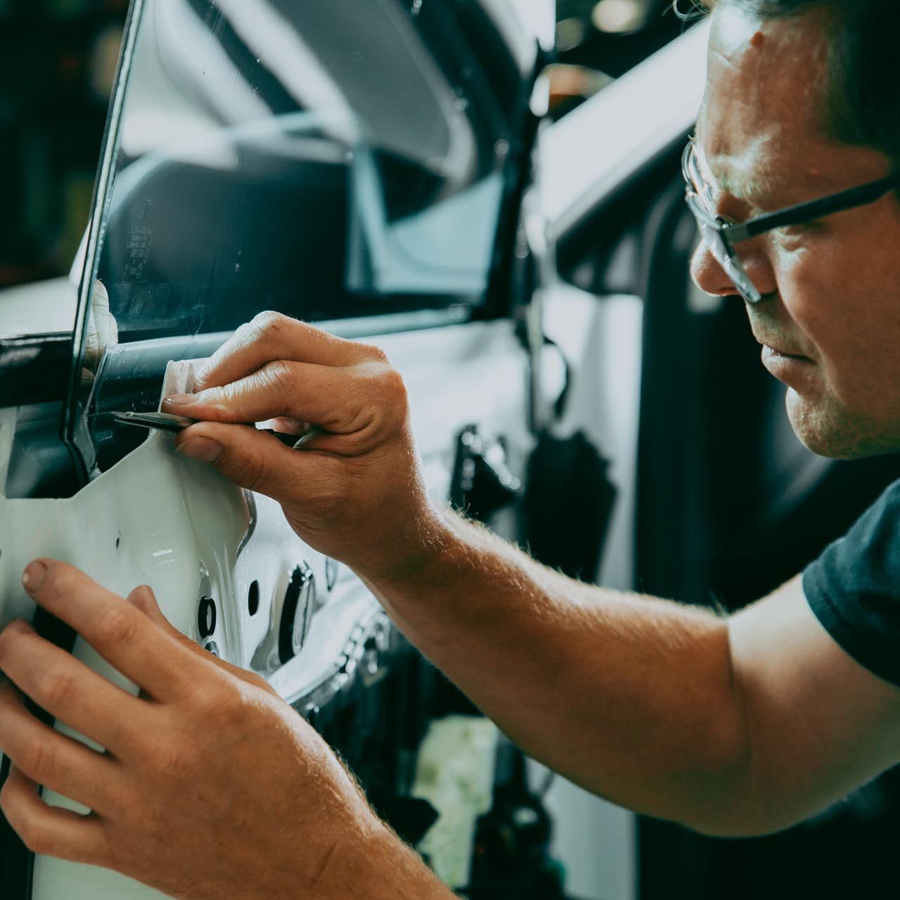 A man wearing glasses is working on a car door